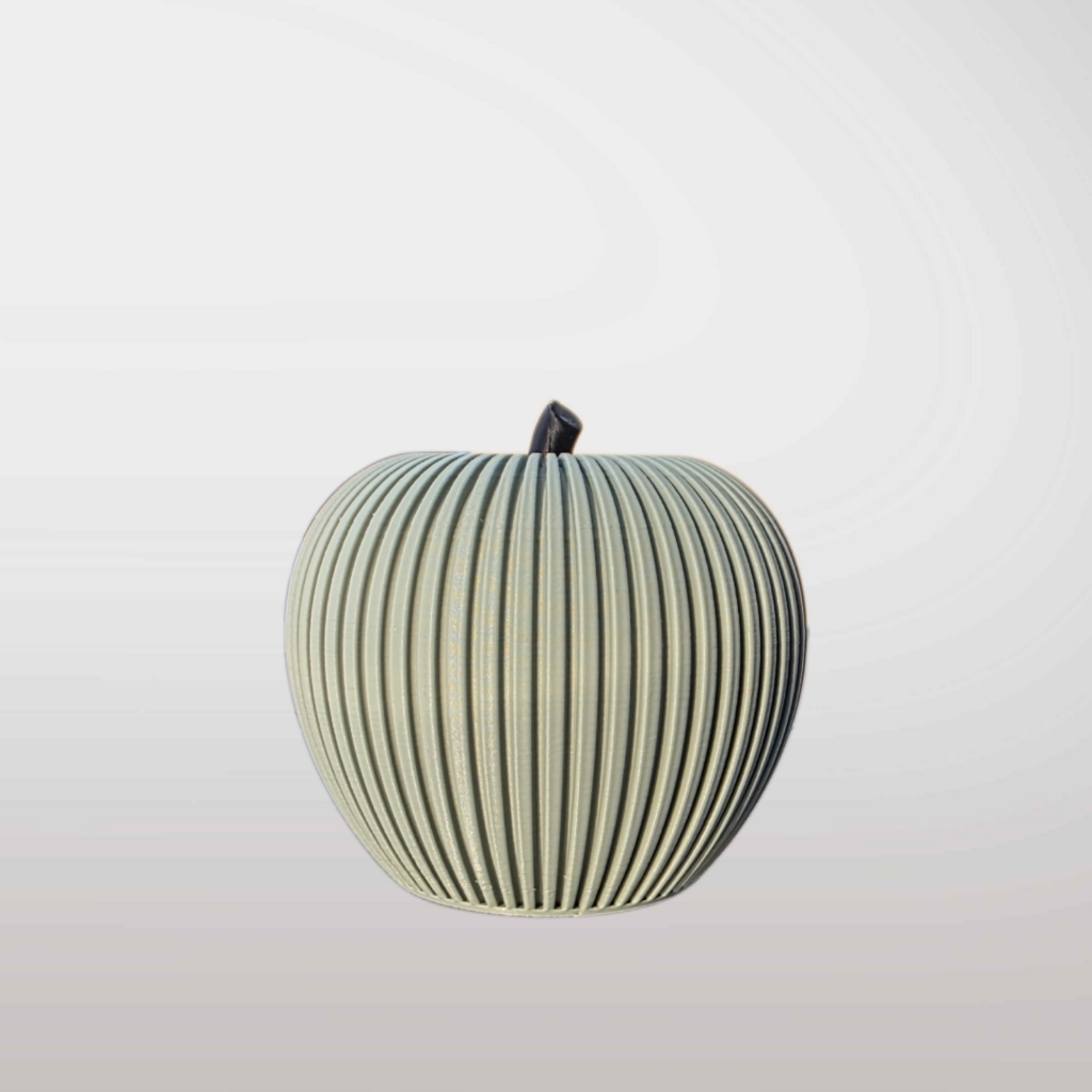 Grüner Deko-Apfel mit vertikaler Rillenstruktur und braunem Blatt im minimalistischen Japandi-Stil auf hellem Hintergrund.